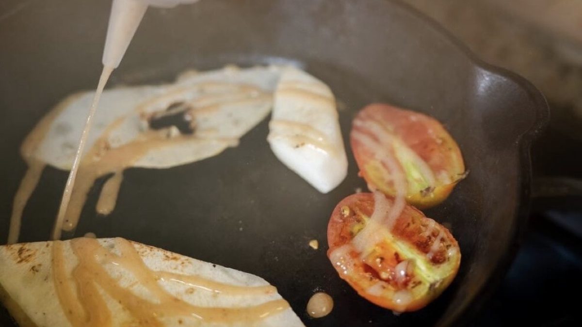 Fish fillets and tomatoes searing in a cast-iron skillet as sauce is drizzled over them