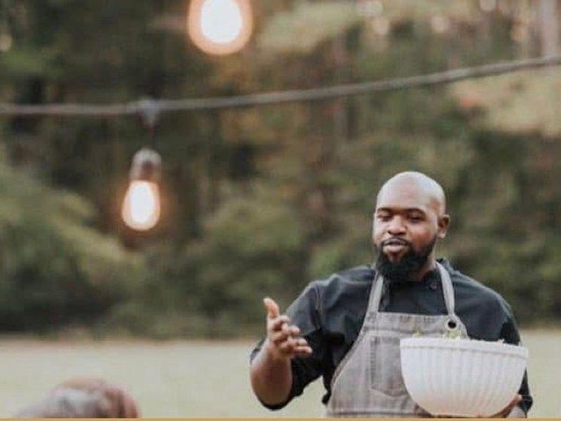 A chef presenting a dish at an outdoor farm dinner under string lights